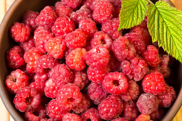 Fresh organic healthy raspberry with mint leaves in clay dish on wooden table background. Rustic style and natural light. food photo.