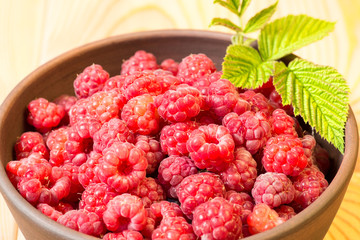 Fresh organic healthy raspberry with mint leaves in clay dish on wooden table background. Rustic style and natural light. food photo.