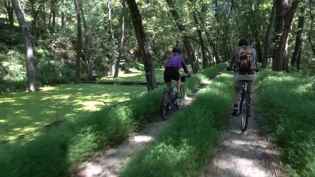 Mature daughter bikes next to her elderly father on the forested C&O Canal, a National Park near Harpers Ferry, West Virginia.