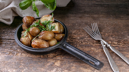 Baked potatoes in a frying pan with basil. Wooden background