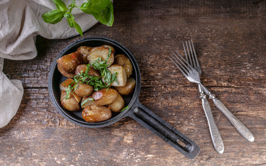 Baked potatoes in a frying pan with basil. Wooden background. Top view