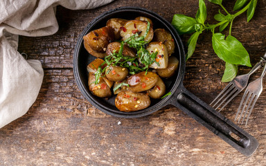 Baked potatoes in a frying pan with basil. Wooden background. Top view