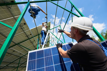 Professional workers team installing solar panels on the green metal construction using different equipment. Innovative solution for energy solving. Use renewable resources. Green energy.