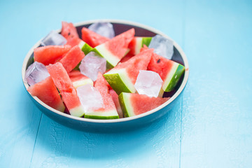 slices of watermelon in a plate with ice on a blue background