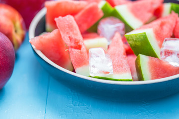 slices of watermelon in a plate with ice and peaches on a blue background