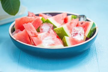 slices of watermelon in a plate with ice on a blue background