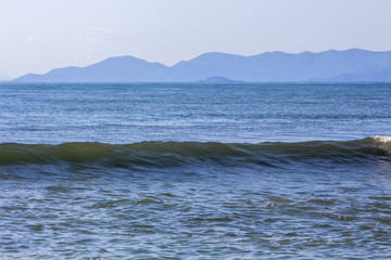 Exciting harmony with a perfect wave against the backdrop of misty hills. Aegean Sea in Asprovalta, Greece.