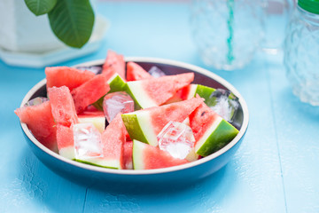 slices of watermelon in a plate with ice on a blue background