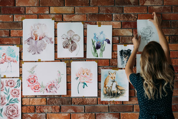 art studio workspace. painter artwork. woman sticking watercolor drawings of flowers and animals to...
