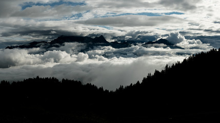 mountain landscape hidden in spectacular cloudscape with forest in the foreground