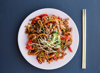 Tasty plate of wok: beef noodles with vegetables and microgreen on the dark background