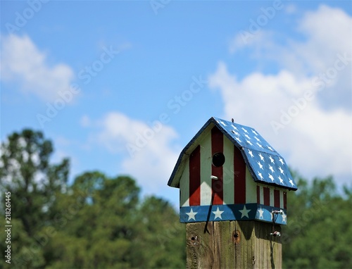 An American Flag Design On The Bird House Is On The Wooden Pole
