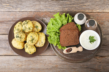Boiled potatoes in plate with bread and sour cream on wooden table