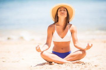 Fototapeta na wymiar Meditation. Yoga woman meditating at serene beach. Girl relaxing in lotus pose in calm zen moment in the ocean water during yoga holidays resort retreat. Multiracial girl.