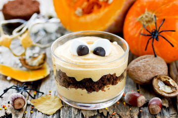 Halloween monster dessert with marshmallow eyes from pumpkin cream and crushed chocolate cookies in...