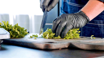 A chef in black gloves chops parsley on wooden board