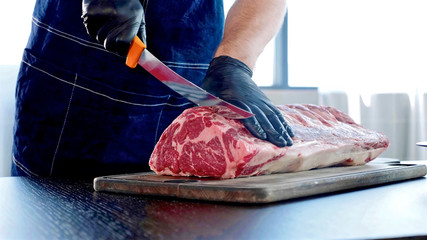 Chef cuts raw meat on the wood board with the knife, close-up