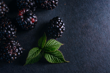 Fresh blackberries, close-ups on a dark background with a green leaf. Top view, flat lay