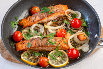 Salmon fried in a pan with onions, lemon and cherry tomatoes