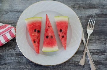  Sliced watermelon on white dish on wood background.