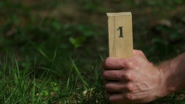 The man's hand drives a wooden stake at number one into the ground