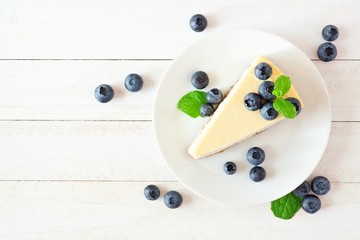 Slice of cheesecake with blueberries. Top view scene over a bright, white wood background.