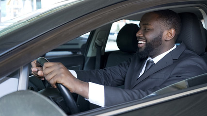 African American man sitting in expensive car satisfied and smiling, test drive