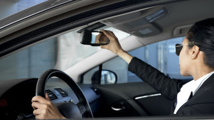 Business lady looking in rear-view mirror, driving automobile, traffic rules