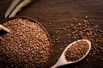 Buckwheat in a wooden bowl on a wooden background near the ears of wheat. wooden spoon with Buckwheat