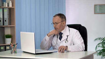 Thoughtful doctor reading information on laptop, thinking on patient diagnosis