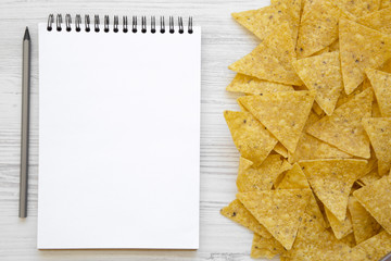 Tortilla chips with blank notebook on white wooden table, top view. Mexican food. Flat lay, from above, overhead. Space for text.