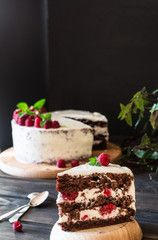 Portion of layered creamy fruit cake with in close up view. Raspberry cake with chocolate. Chocolate cake. Mint decoration. Cheesecakeon wooden table and dark background. Still life of food.