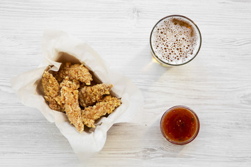 Top view chicken strips with sauce and cold beer on a white wooden table. Overhead, from above.