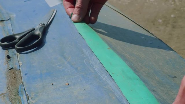 Process of reparing canoe. Man tapes hole on bottom of canoe