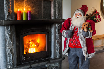 Fireplace made of black stone with fire and burning multicolored candles on a shelf and Santa Claus