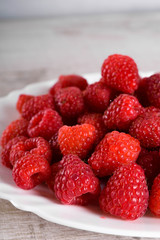 Red fresh raspberries on white rustic wood background. Plate with natural ripe organic berries.flat lay with copy space
