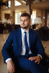 Fototapeta premium groom at wedding tuxedo smiling and waiting for bride in the hall of the hotel . Rich groom at wedding day. Elegant groom in costume and bow-tie. Groom in a suit holding buttonhole.