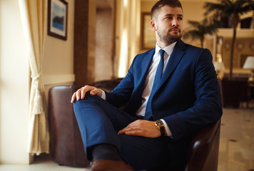 groom at wedding tuxedo smiling and waiting for bride in the hall of the hotel . Rich groom at wedding day. Elegant groom in costume and bow-tie. Groom in a suit holding buttonhole.