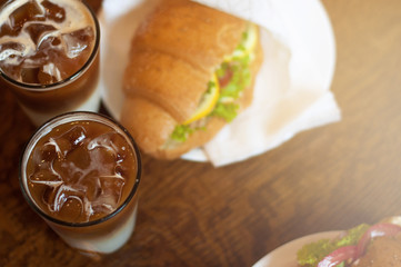 croissant sandwiches and ice coffee cups on wooden table