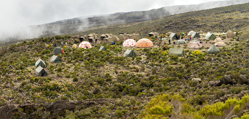 Campsite with many tents and domes on a grass and shrub hillside with mist and clouds