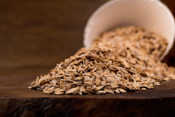 Crumbled from a white bowl of oat flakes on a wooden table, close-up.
