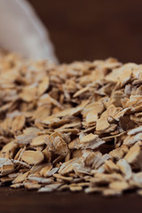 Oat flakes on a wooden background, scattered from an overturned porcelain bowl.