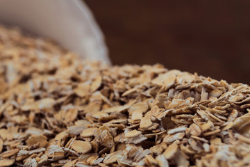 Crumbled white bowl oat flakes close up on wooden background.
