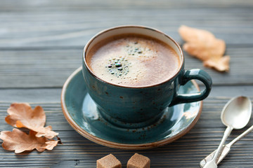 Blue cup whith coffee, knitted sweater, autumn leaves on wooden background. Cozy morning.