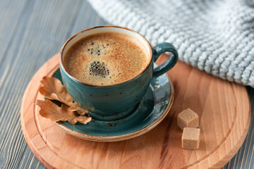 Blue cup whith coffee, knitted sweater, autumn leaves on wooden background. Cozy morning.