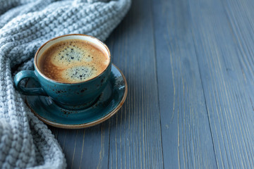Blue cup whith coffee, knitted sweater, autumn leaves on wooden background. Copy space.