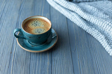Blue cup whith coffee, knitted sweater, autumn leaves on wooden background. Copy space.