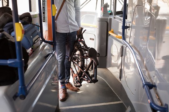 Male commuter with folding bicycle entering in modern bus
