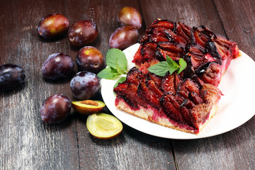 Rustic plum cake on wooden background with plums around.