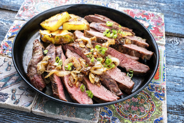 Barbecue dry aged wagyu flank steak with pineapples and onion rings as closeup on a plate